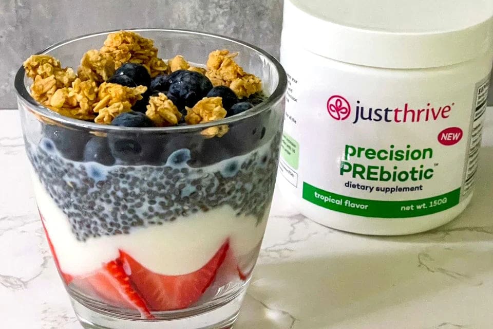 a glass of yogurt with berries and granola in front of a jar