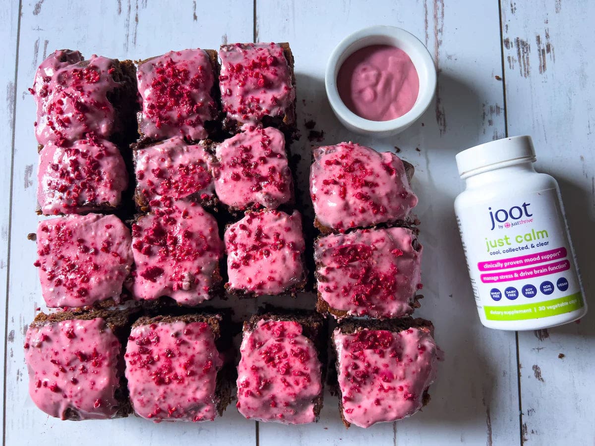 a group of brownies with pink frosting next to a container of yogurt